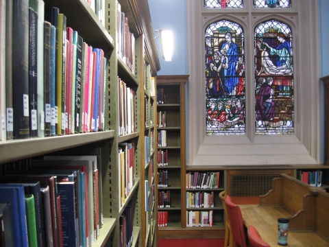 One of the aisles of the library with the stained glass in the background.